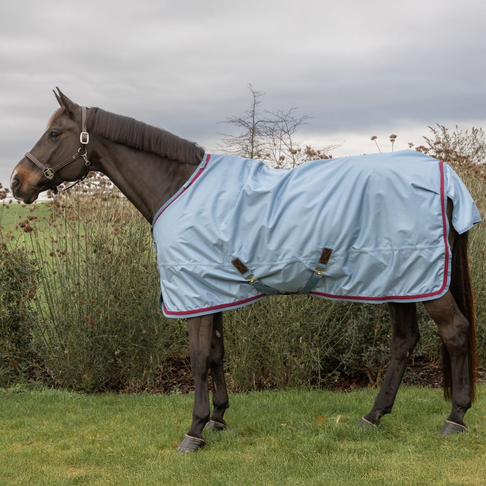 KENTUCKY® HORSEWEAR Weidedecke All Weather Waterproof Pro 160 g, denim Wasserdichte Allwetter-Ausreitdecke Pro in Denim-Blau mit roter Borte und Kreuzgurten am braunen Pferd, Seitenansicht.