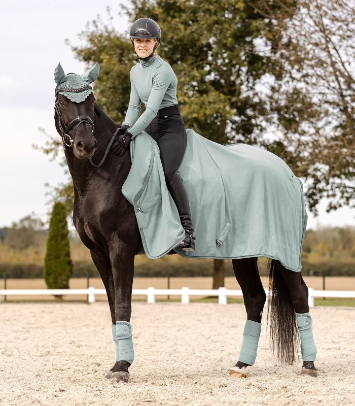 WALDHAUSEN Fliegenohren Nepal, silberblau Ein Rappe mit Reiterin trägt die silberblauen WALDHAUSEN Fliegenohren Nepal und eine passende Ausreitdecke.