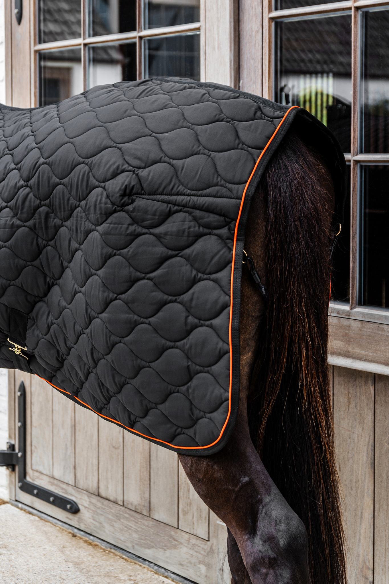 KENTUCKY® HORSEWEAR Stalldecke Wave 160g, schwarz Schwarze Stalldecke Wave mit wellenförmiger Steppung und oranger Paspel auf dem Rücken eines dunklen Pferdes.