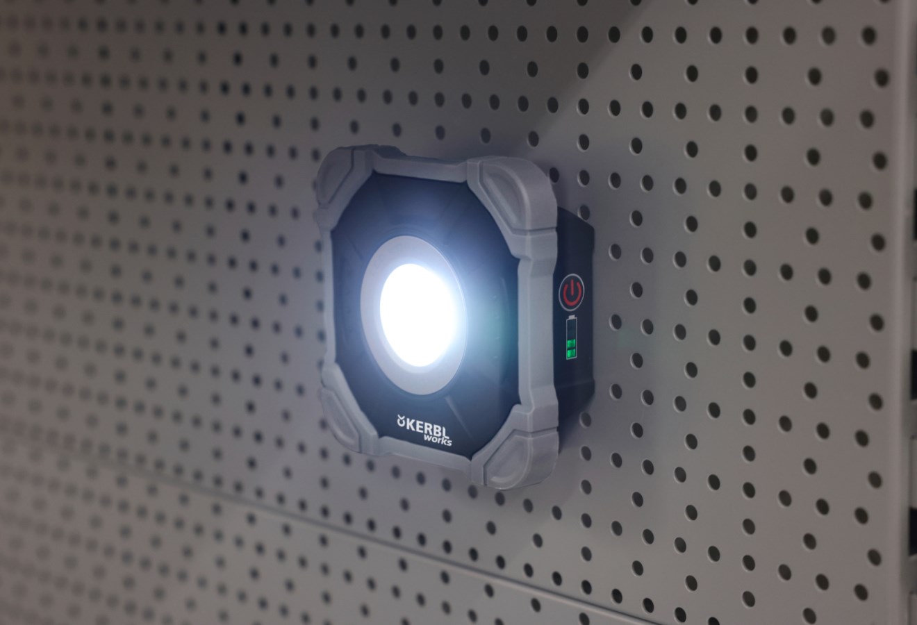 Mobiler Kerbl LED-Strahler WorkFire 2200 in Schwarz-Grau, leuchtend und magnetisch an einer Lochwand befestigt.