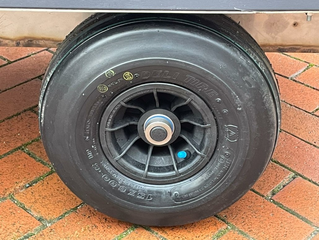 Detailaufnahme des schwarzen Reifens am Heubedampfer mit Kunststofffelge und blauer Ventilkappe auf Pflaster.