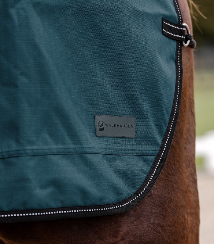 Nahaufnahme der petrolblauen Regen-Nierendecke Salzburg mit Waldhausen-Logo und reflektierender Paspel.