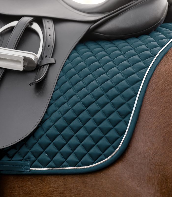 Waldhausen Dressur-Schabracke Felix Glam in Petrolblau mit Rautensteppung und silberner Zierkordel unter einem Sattel.