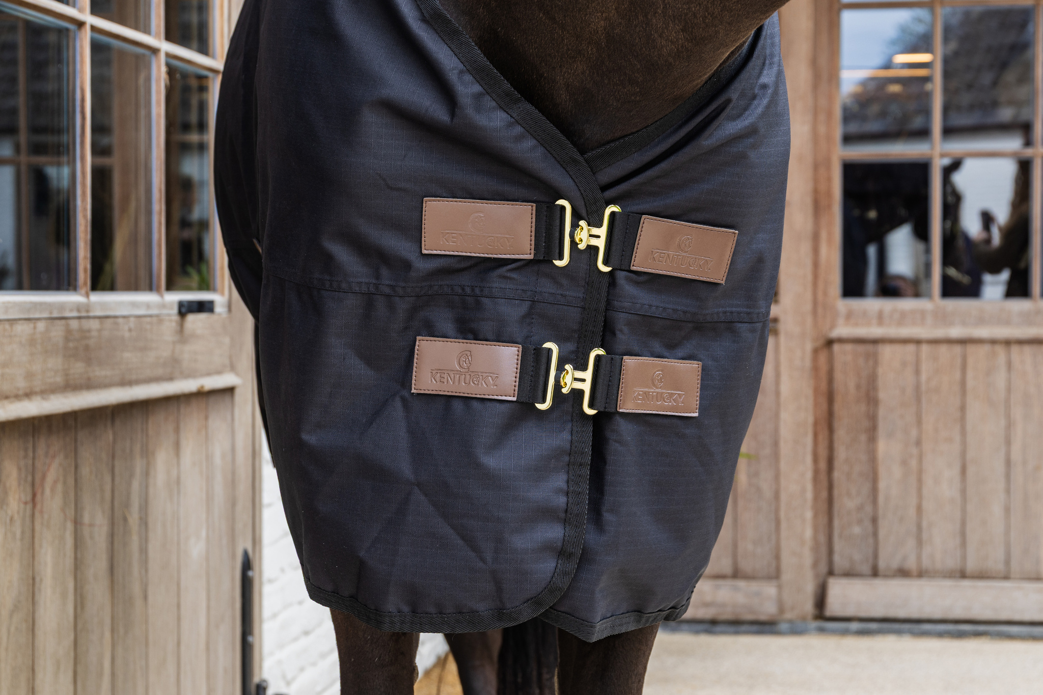 KENTUCKY® HORSEWEAR Winterdecke All Weather Waterproof Classic 0 g, schwarz Detailansicht der schwarzen All Weather Weidedecke Classic mit zwei goldenen Brustverschlüssen und Logo-Patches.