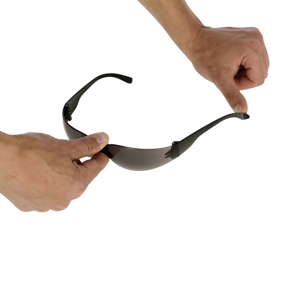 Hände biegen die flexible Schutzbrille Light mit schwarzem Kunststoffrahmen und getönten Sichtscheiben.