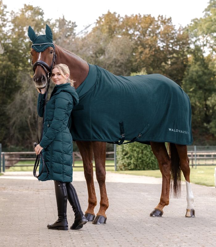 WALDHAUSEN NEPAL Fleecedecke - petrolblau Braunes Pferd trägt die petrolblaue Nepal Fleecedecke und eine passende Fliegenhaube, daneben steht die Reiterin.