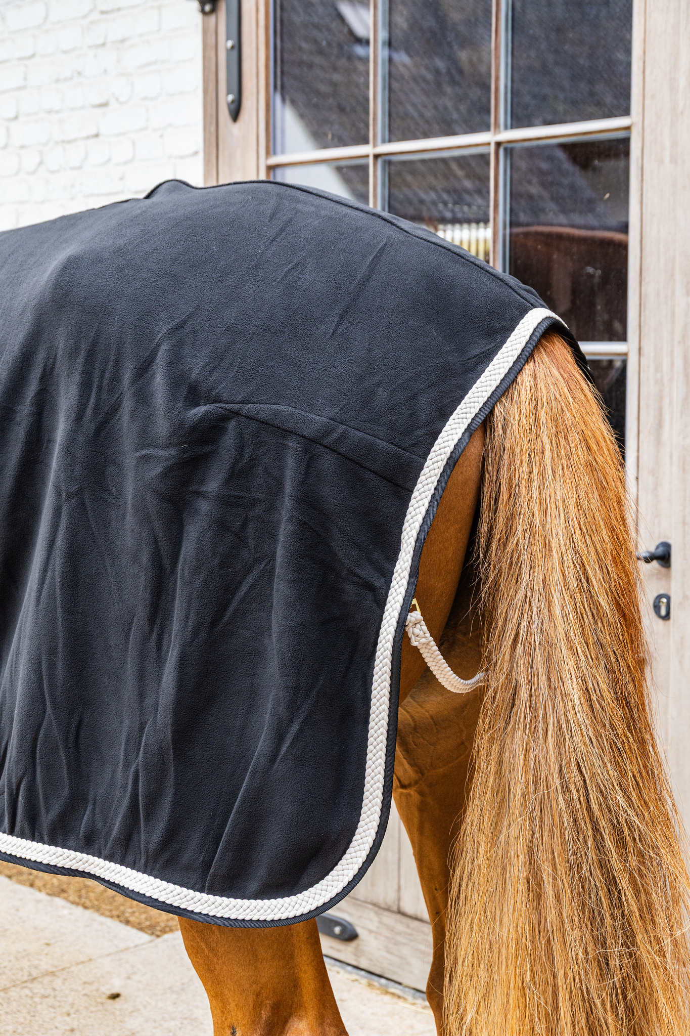 KENTUCKY® HORSEWEAR Abschwitzdecke Fleece geflochtene Kordel, schwarz Rückansicht der schwarzen Fleece-Abschwitzdecke mit weißer, geflochtener Zierkordel und Schweifkordel am Pferd.