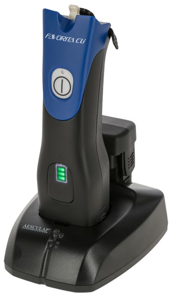 Blaue Aesculap Akkuschermaschine Favorita CLi ohne Scherkopf in der schwarzen Ladestation mit leuchtender Akkuanzeige.