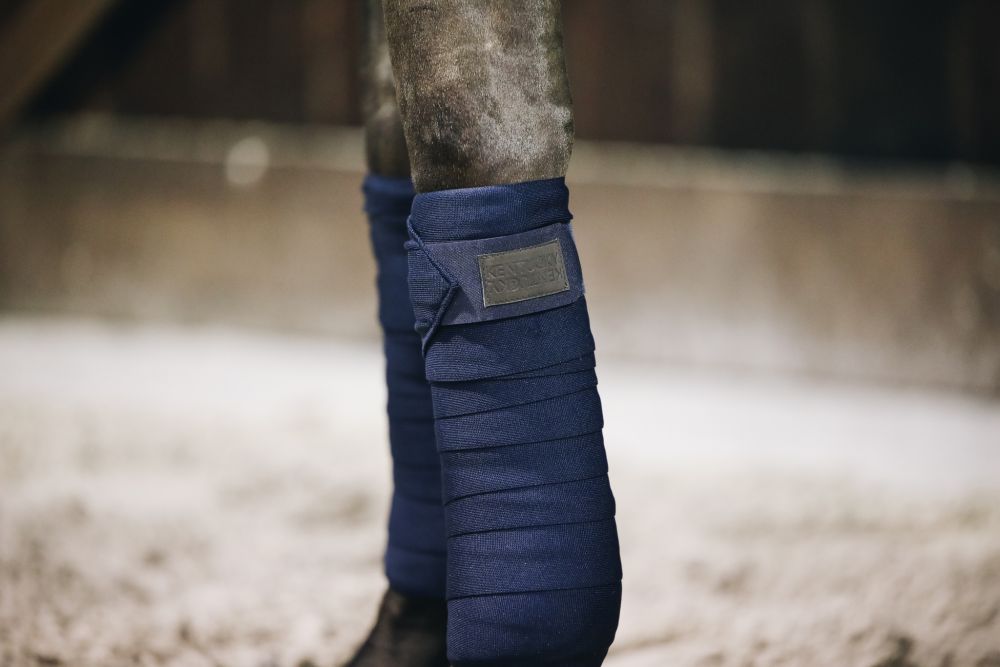Nahaufnahme der Kentucky Horsewear Repellent Arbeits-Bandagen in Marine, um die Beine eines Pferdes gewickelt.