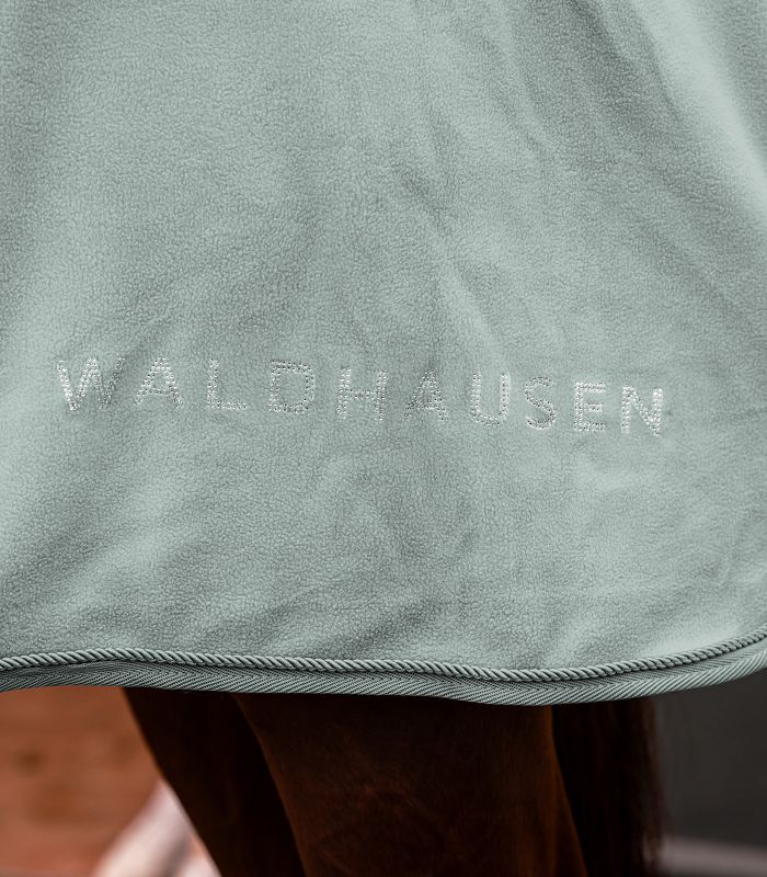 WALDHAUSEN NEPAL Fleecedecke - silberblau Detailansicht der Nepal Fleecedecke in silberblau mit gesticktem Waldhausen Schriftzug und Zierkordel am Rand.