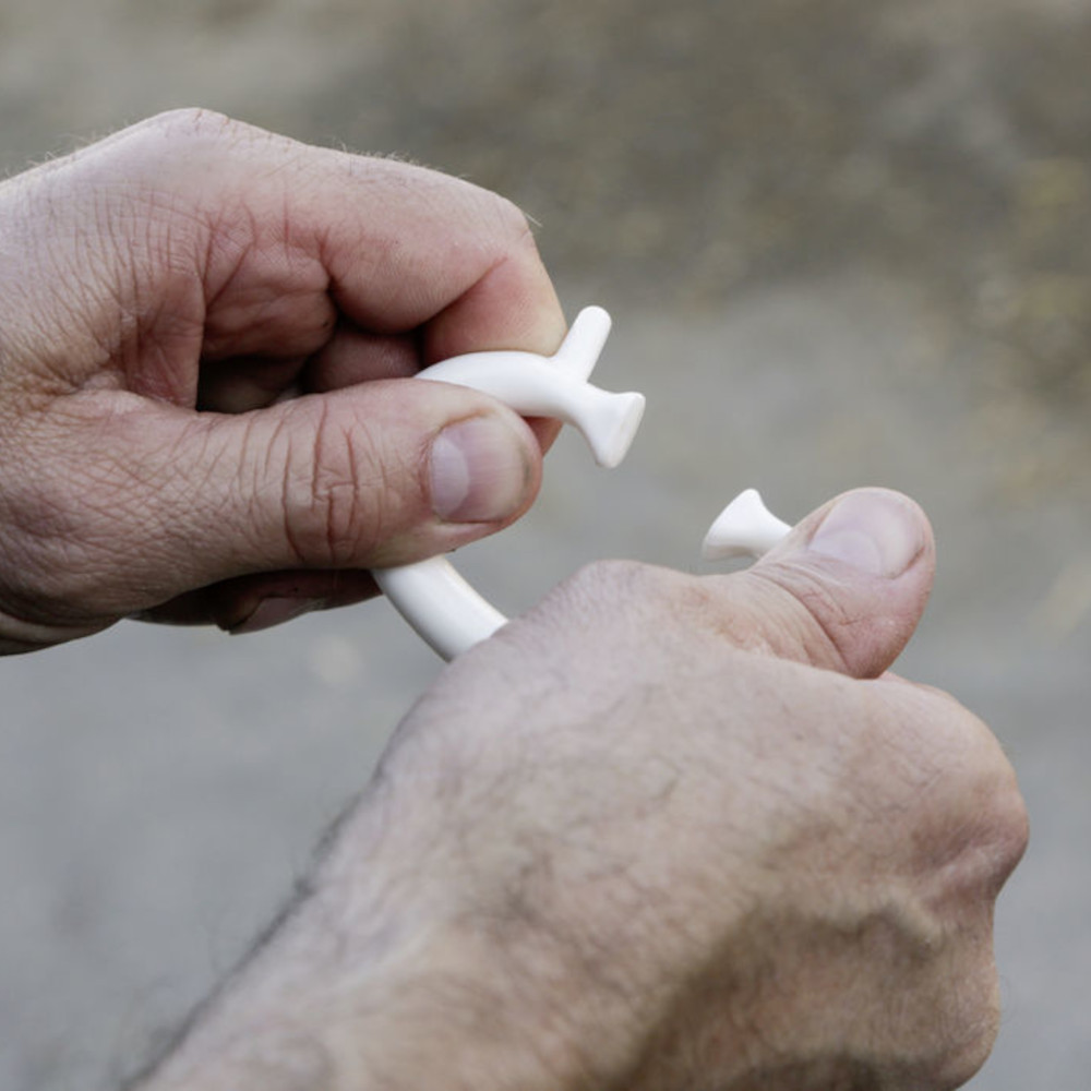 Viehsaugentwöhner SuckStop Müller Hände demonstrieren das Öffnen des weißen SuckStop Mueller Viehsaugentwöhners aus flexiblem Kunststoff.