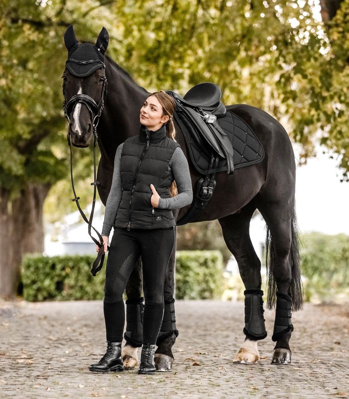 Eine Reiterin steht neben ihrem gesattelten Rappen, der die schwarze WALDHAUSEN Schabracke Competition Dressur trägt.