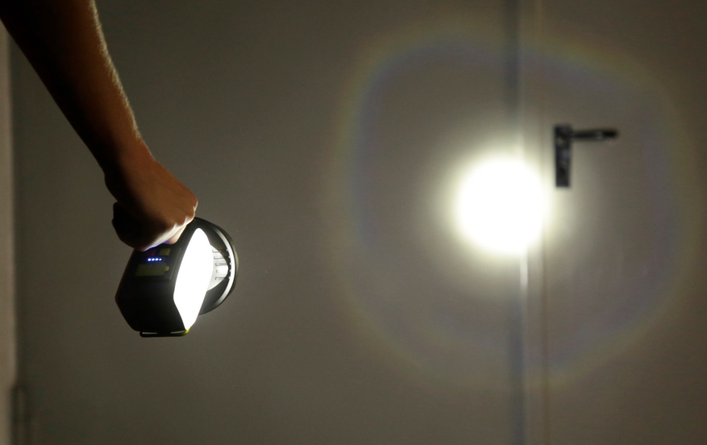 Schwarzer LED Akku-Handscheinwerfer im Einsatz, der mit seinem hellen Lichtkegel eine Tür im Dunkeln anstrahlt.