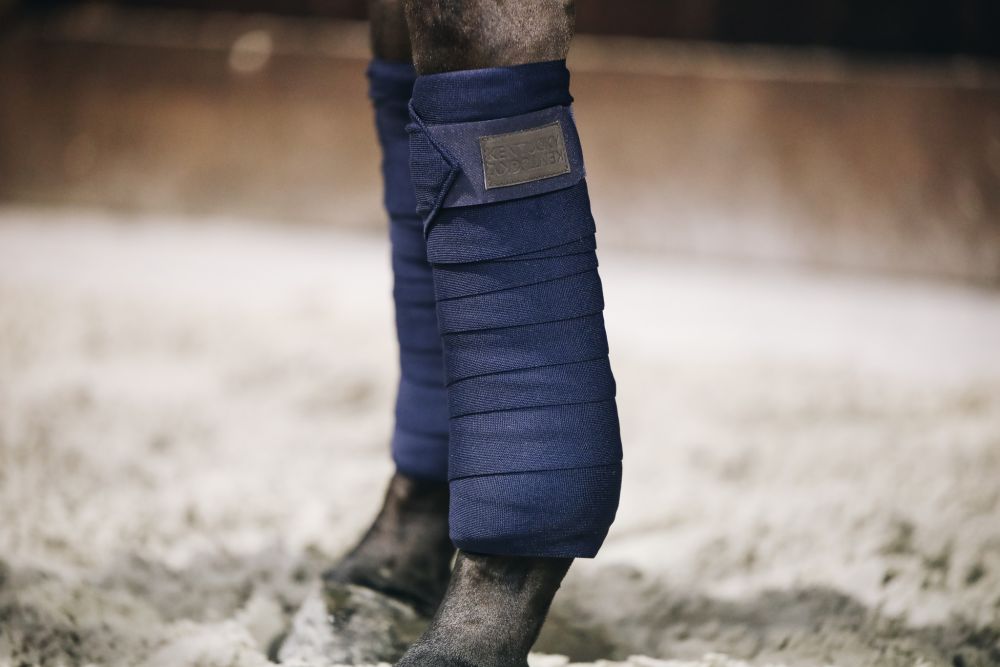 Marineblaue Repellent Arbeits-Bandagen von Kentucky Horsewear am Bein eines Pferdes im Sand.