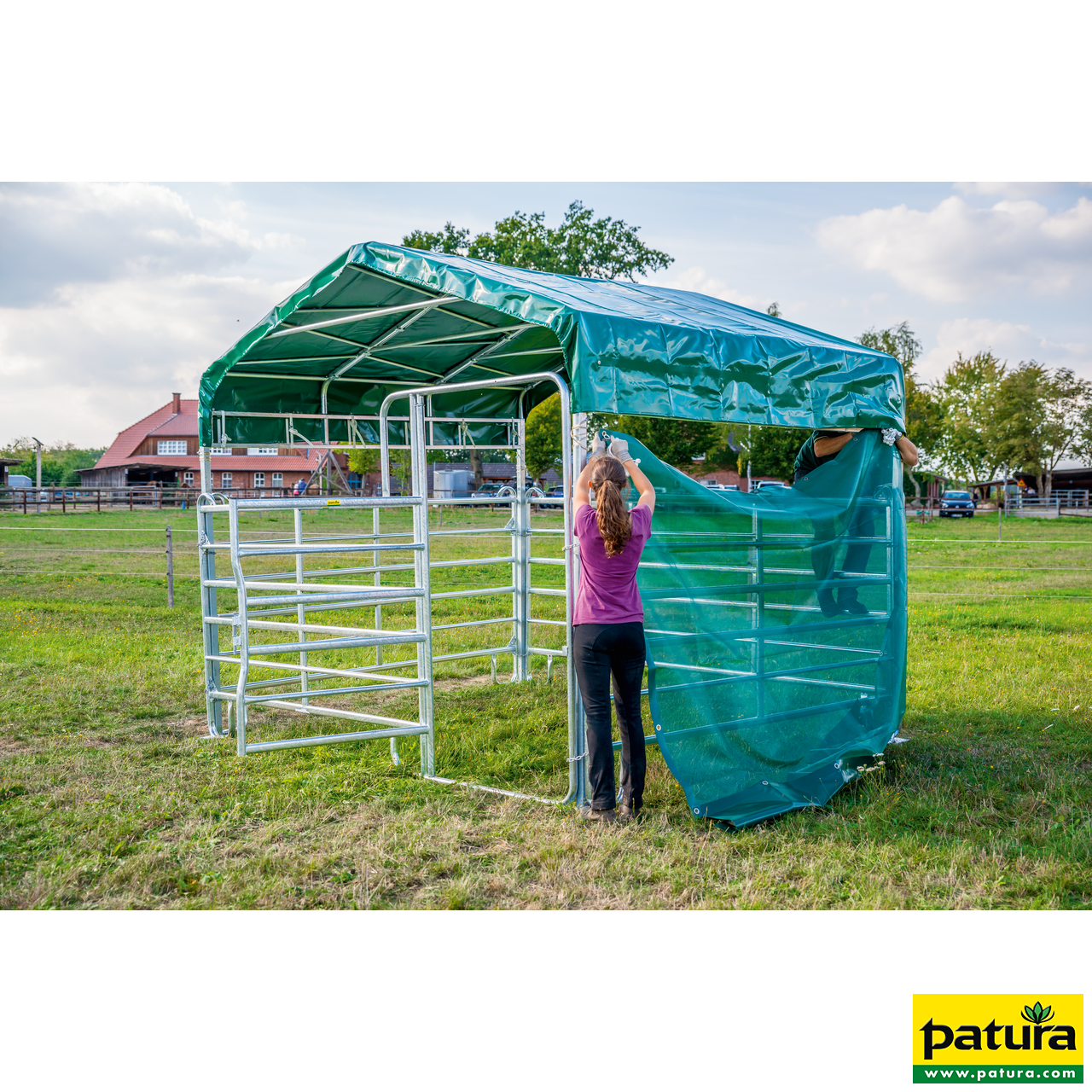 PATURA Weidezelt Profi Panel-Dach für einen Weideunterstand im Aufbau. Eine Frau befestigt ein grünes Windschutznetz an den verzinkten Panels.