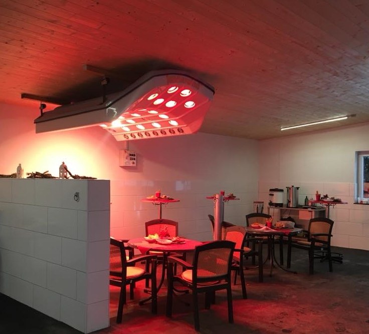 SUMMERWIND Pferdesolarium Premium Summerwind Pferdesolarium Premium mit eingeschalteten Infrarotlampen, montiert an einer Holzdecke über einem gefliesten Bereich.