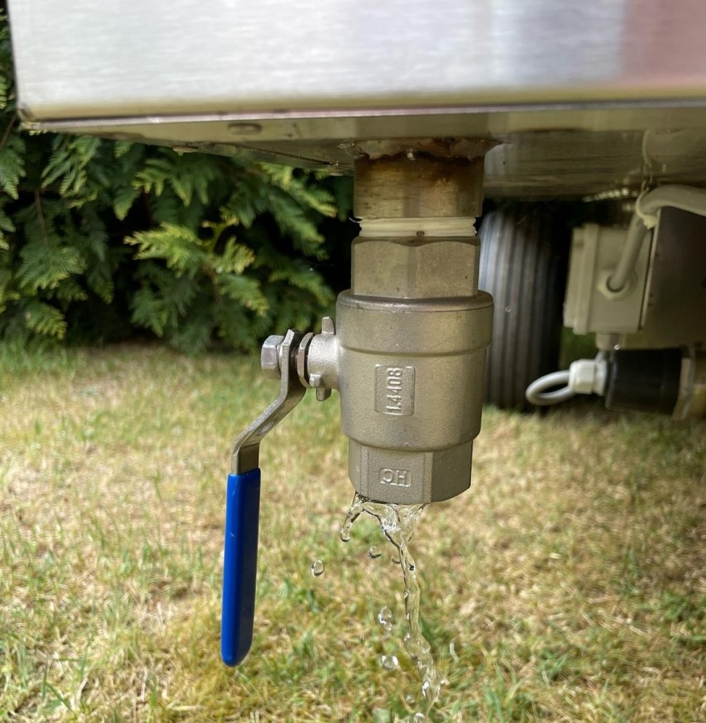 Detailansicht eines silbernen Ablasshahns mit blauem Hebel, der an einem Behälter montiert ist und Wasser ablässt