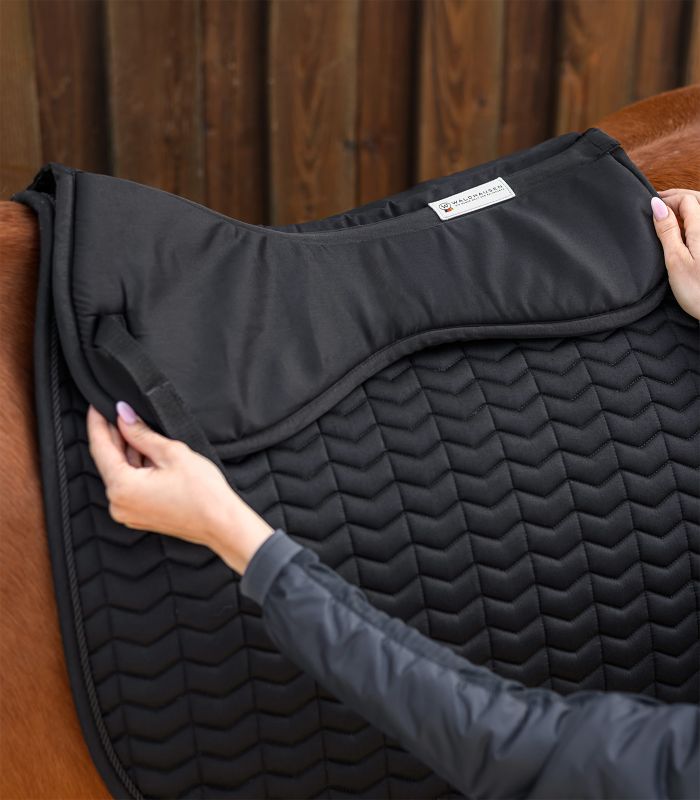 WALDHAUSEN Sattelkissen Memory Foam Schwarzes Waldhausen Sattelkissen aus Memory Foam mit V-Steppung wird von Händen auf einen Pferderücken gelegt.