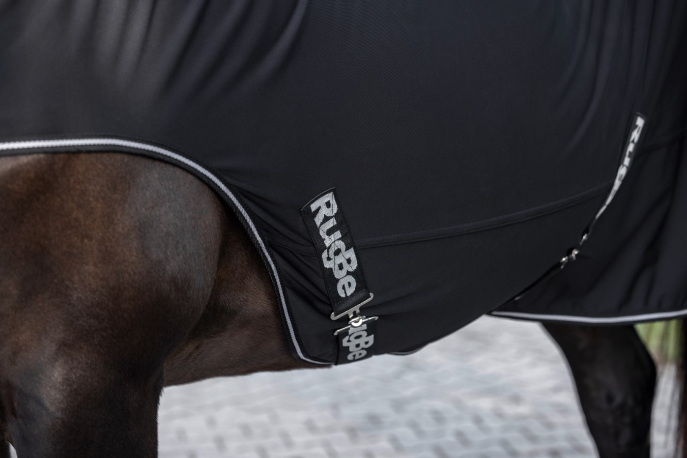 Schwarze Kerbl Führanlagendecke RugBe aus Funktionsmaterial mit Bauchgurt und Logo-Print am Pferd.