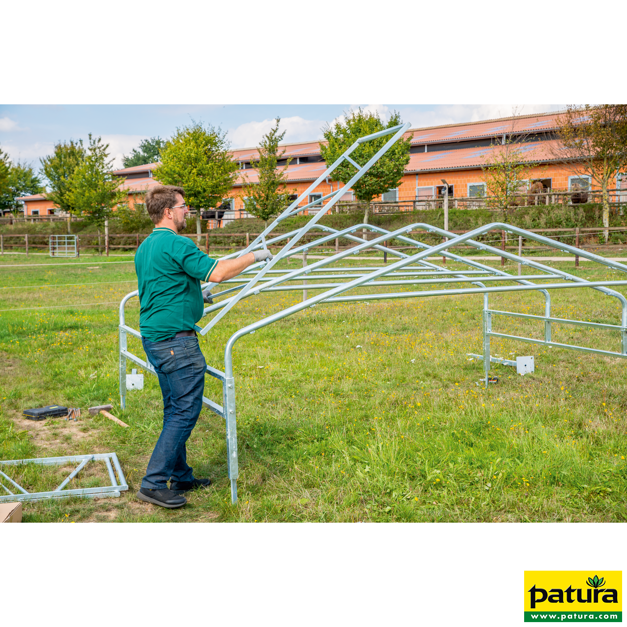 PATURA Weidezelt Profi Ein Mann montiert auf einer grünen Wiese den verzinkten Stahlrahmen für ein Panel-Dach als Weideunterstand.
