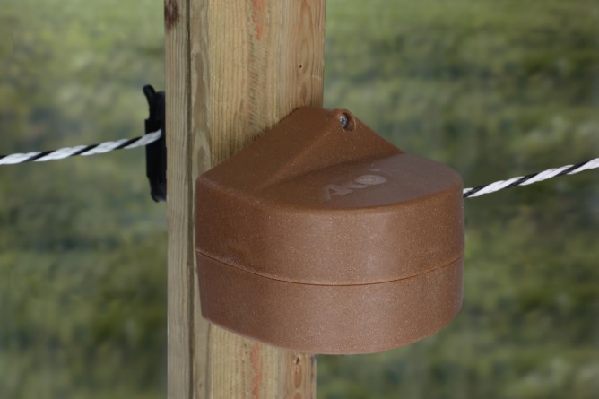 AKO Tor-Set Premium FLEXIGATE mit braunem Kunststoffgehäuse, montiert an einem Holzpfosten für einen Weidezaun.