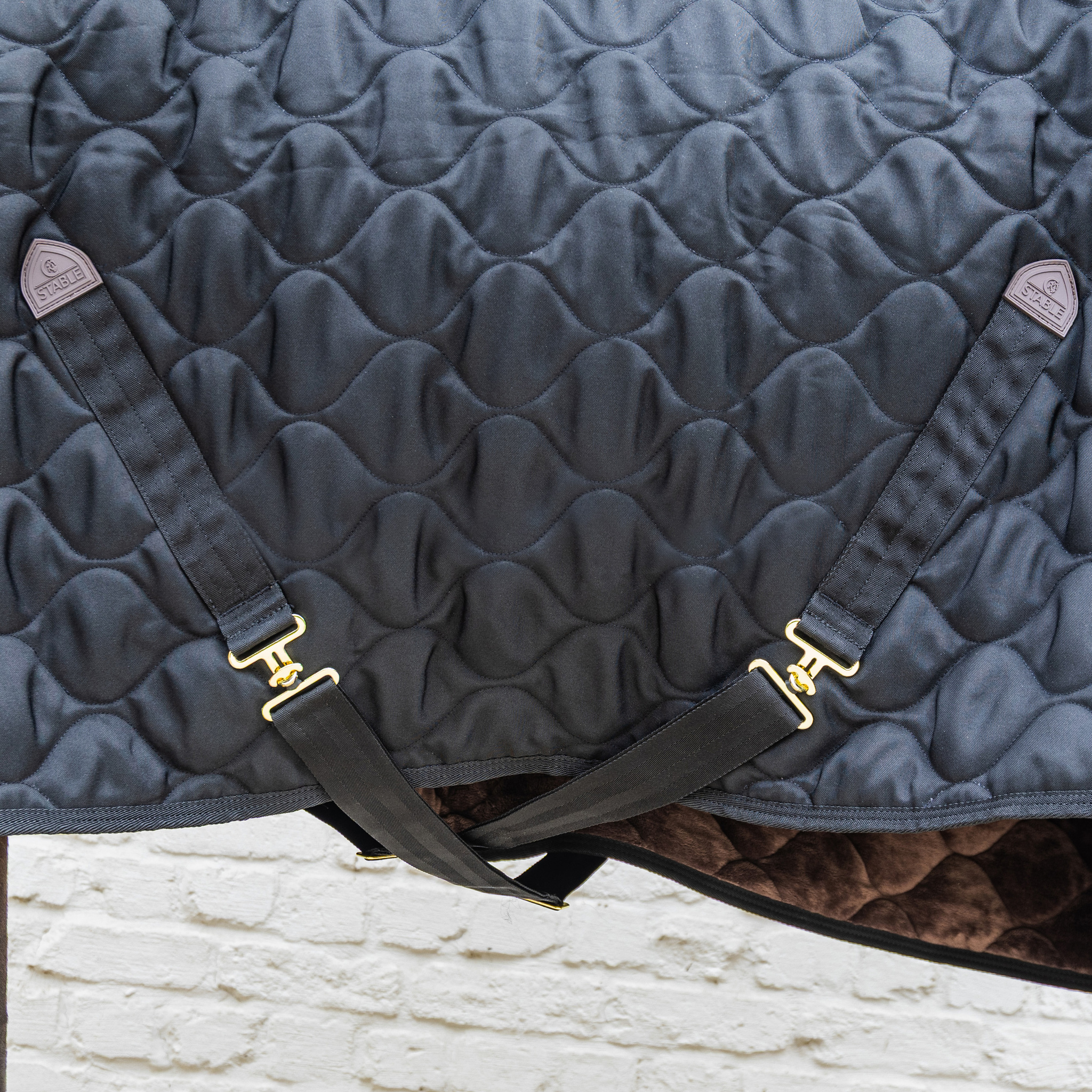KENTUCKY® HORSEWEAR Stalldecke Comfort 300 g, schwarz Nahaufnahme der schwarzen Stalldecke Comfort mit Wellensteppung, Kreuzbegurtung und goldfarbenen T-Verschlüssen.