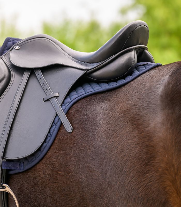 Blaue WALDHAUSEN Satteldecke Star Vielseitigkeit, gesteppt, unter einem schwarzen Ledersattel auf einem Pferderücken.