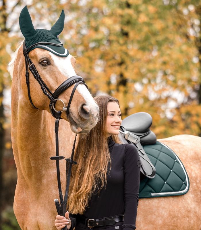 Ein Palomino trägt die tannengrüne WALDHAUSEN Schabracke Competition Dressur mit silberner Biese und Fliegenhaube.