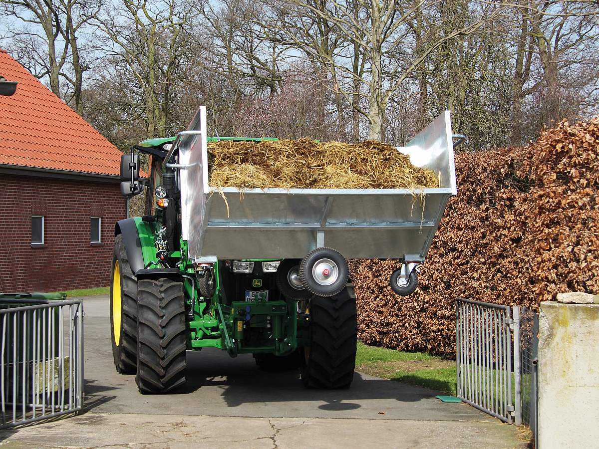 GROWI Großraumkuli für Traktoren, verzinkt und mit Stroh beladen, an der Heckhydraulik eines grünen Traktors.