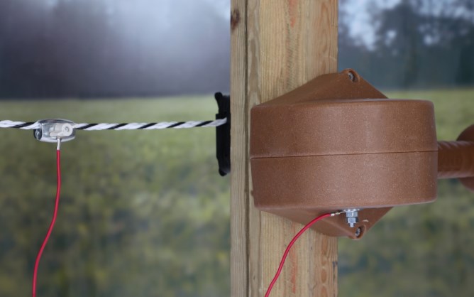 Nahaufnahme des AKO FLEXIGATE Tor-Sets an einem Holzpfosten. Das braune Gehäuse ist mit dem schwarz-weißen Seil verbunden.