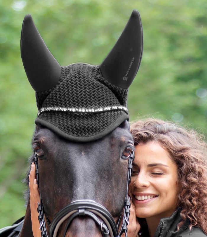 WALDHAUSEN Fliegenohren Quiet, schwarz Schwarze Waldhausen Fliegenohren Quiet mit Strasssteinen am Kopf eines Pferdes, das von einer Frau gehalten wird.