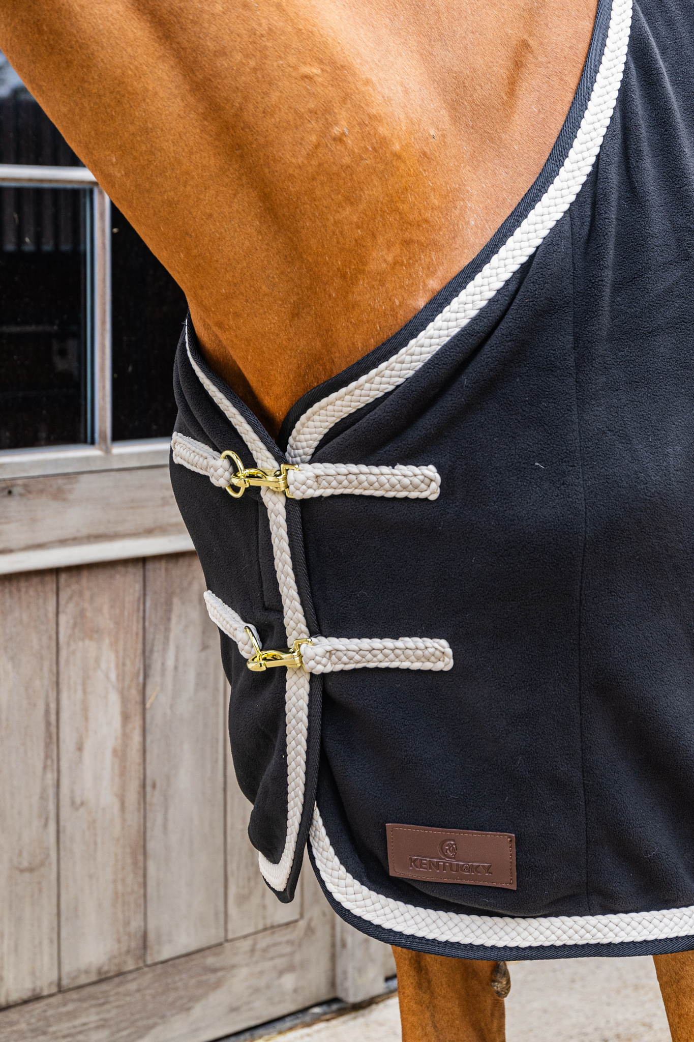 KENTUCKY® HORSEWEAR Abschwitzdecke Fleece geflochtene Kordel, schwarz Detailansicht der schwarzen Fleece-Abschwitzdecke mit beiger geflochtener Kordel und goldenen Brustverschlüssen.