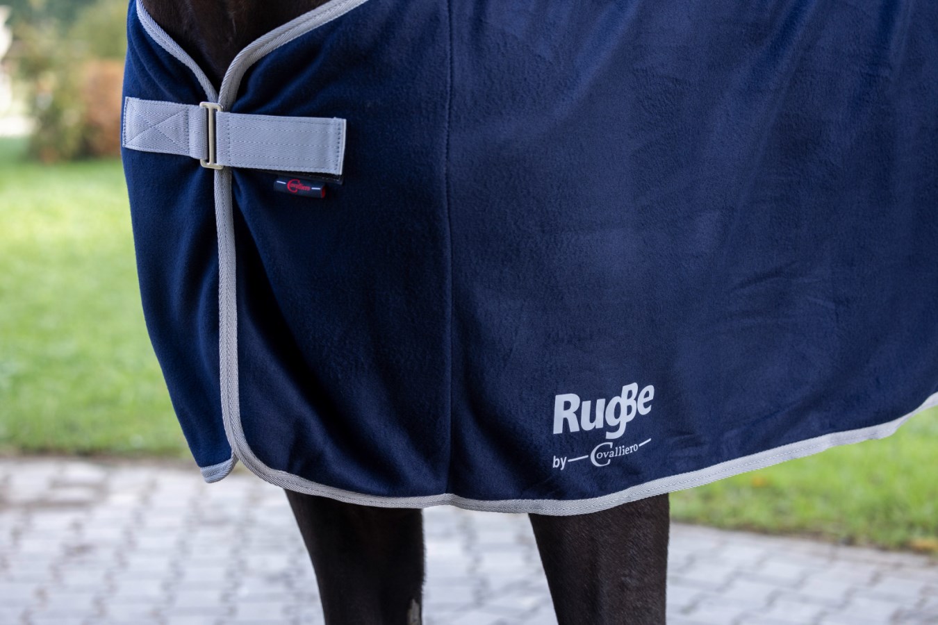 Dunkelblaue KERBL RugBe Fleecedecke Economic am Pferd mit grauem Brustverschluss und grauer Einfassung in der Seitenansicht.