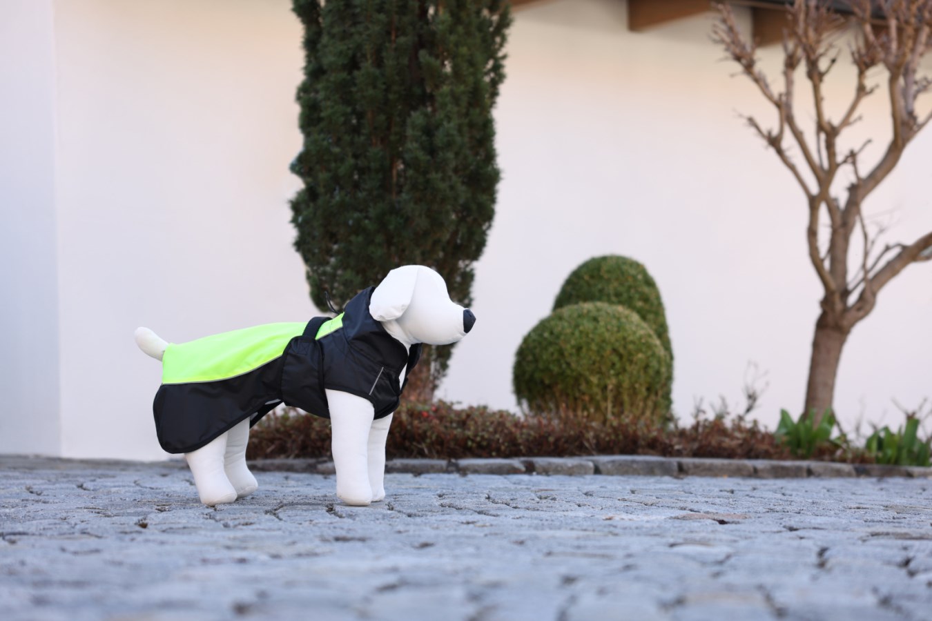 Kerbl Hundemantel Malm in Schwarz und Neongrün mit Kapuze, seitlich an einer Hundepuppe im Freien gezeigt.