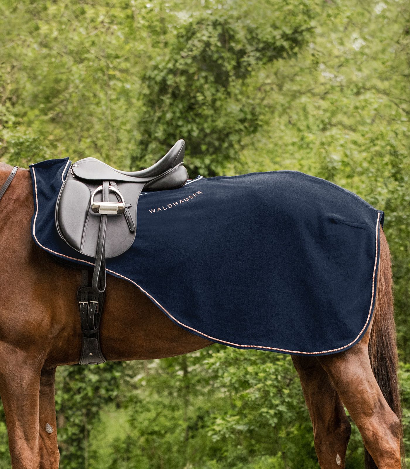 Seitenansicht der nachtblauen Waldhausen Ausreitdecke Modern Ros mit roségoldener Kordel auf einem gesattelten Pferd.